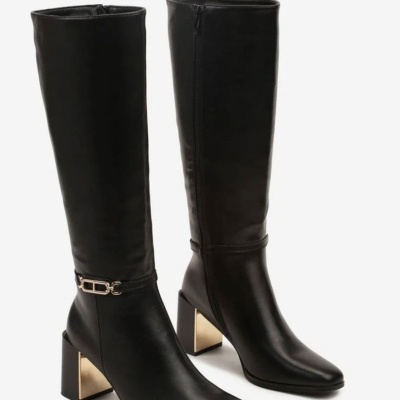 Botas pretas de cano alto em couro com salto dourado e fivela metálica.