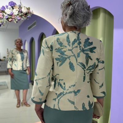 Casaco bege com padrão de folhas azuis e saia verde numa sala com paredes lilás