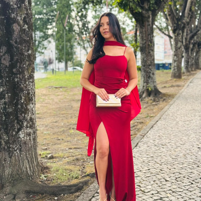Mulher com vestido longo vermelho e carteira dourada, em passeio urbano com árvores.