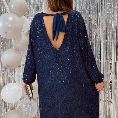 Vestido azul escuro de festa com lantejoulas e detalhe de laço nas costas em cenário festivo.