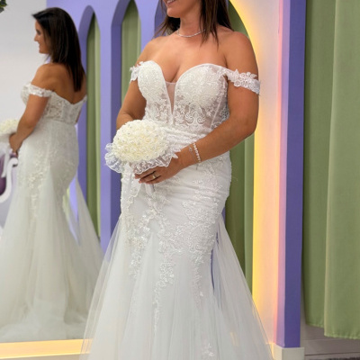 Mulher com vestido de noiva branco com renda e bouquet branco, refletida em espelho decorado com flores