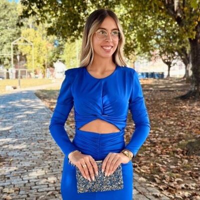 Mulher com vestido azul e clutch azul com padrão brilhante numa calçada de pedra ao ar livre