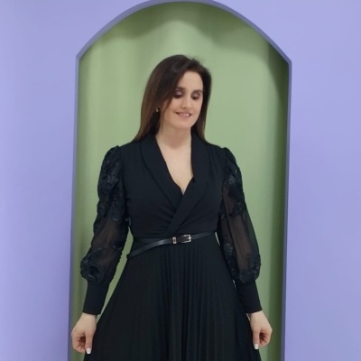 Mulher com vestido preto plissado e mangas transparentes em ambiente interior com paredes coloridas