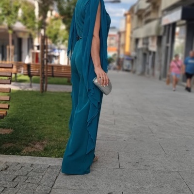 Mulher com vestido azul turquesa e carteira prateada numa rua com bancos e árvores