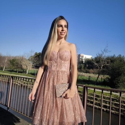 Mulher com vestido rosa cintilante segurando clutch prateada ao ar livre numa ponte