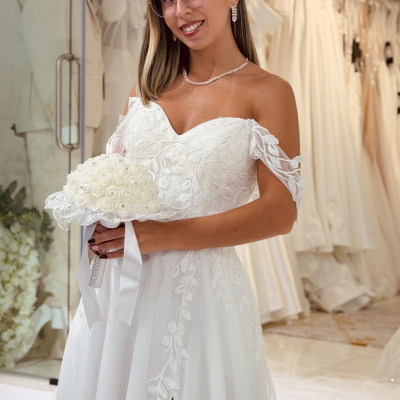 Mulher com vestido de noiva branco e bouquet em loja de vestidos de casamento