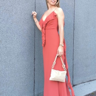 mulher com vestido longo coral e bolsa bege em frente a uma parede cinza
