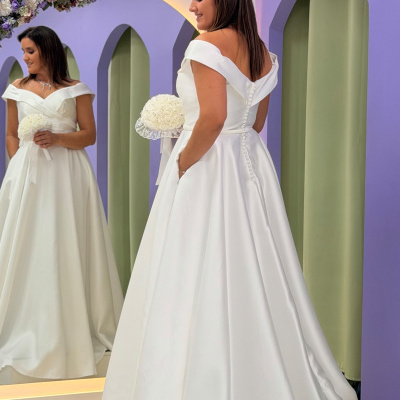 Mulher com vestido de noiva branco refletida em espelho com flores azuis, arco roxo ao fundo