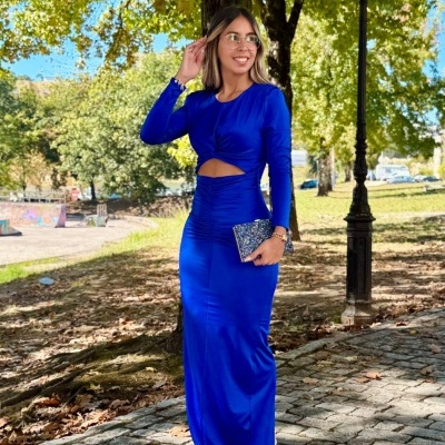 Mulher com vestido azul royal comprido e carteira azul com padrão branco no parque.