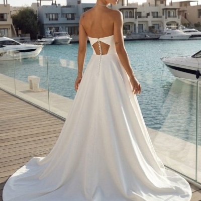 Vestido de noiva branco sem alças, costas descobertas, com botões, num cais com barcos