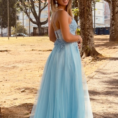 Vestido longo azul claro de tule com aplicações florais no corpete em ambiente exterior.