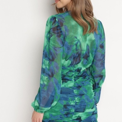 Vestido curto feminino em tons de verde e azul, mangas compridas e detalhe franzido nas costas.