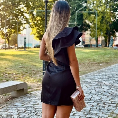 Mulher de costas com vestido preto curto e clutch rosa numa calçada de pedras ao ar livre