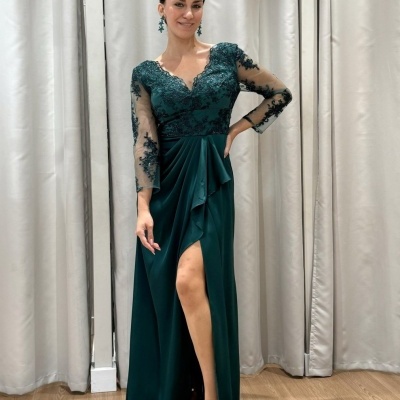 Vestido longo verde escuro com renda e fenda, usado por mulher em interior.