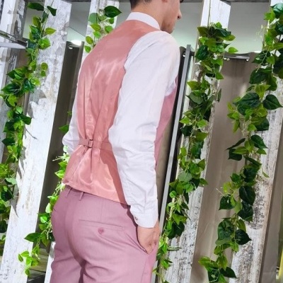 Homem a usar colete rosa e calças cor-de-rosa em ambiente com decoração de plantas e teto de palha