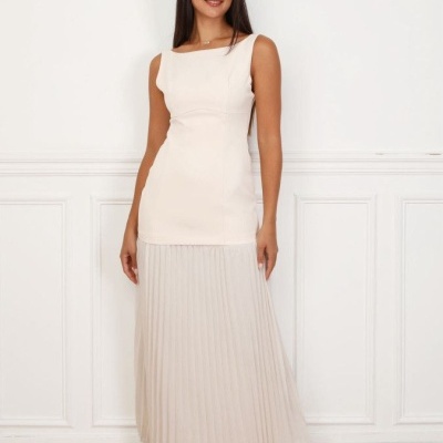 vestido comprido bege claro com saia plissada usado por mulher numa sala com parede branca e chão de madeira