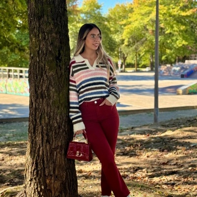 Mulher de camisola às riscas e calças bordeaux junto a árvore