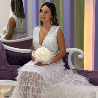 Mulher com vestido de noiva branco com corpete prateado com lantejoulas e saia em tule, sentado num sofá roxo