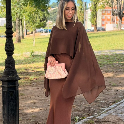 Mulher com vestido castanho longo e carteira rosa em parque exterior