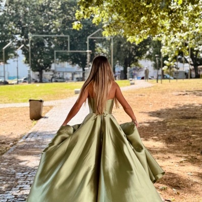 Mulher de costas com vestido longo verde esvoaçante num parque