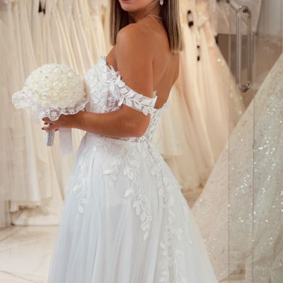 Mulher de costas a usar vestido de noiva branco com renda e a segurar bouquet de flores brancas na loja de vestidos
