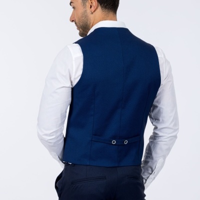 Homem de costas com colete azul escuro, camisa branca e calças escuras