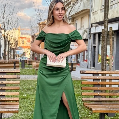 Mulher com vestido verde esmeralda longo em zona urbana com bancos e árvores