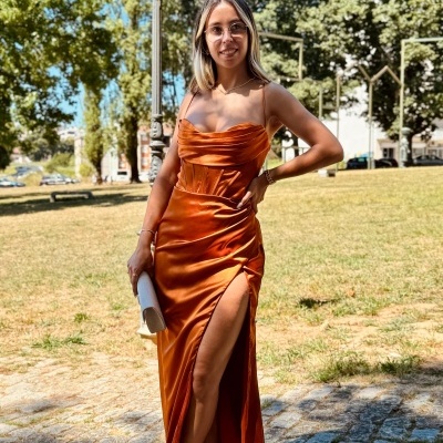 Vestido longo laranja de cetim com fenda alta usado por mulher ao ar livre