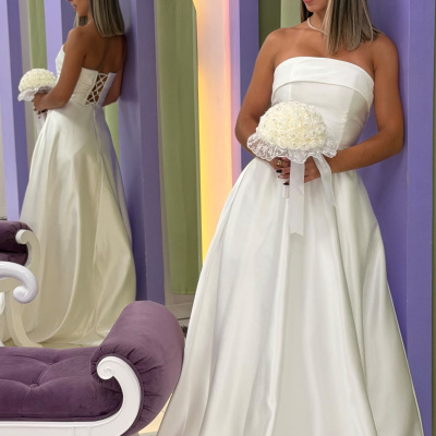 Mulher de vestido de noiva branco segurando bouquet, encostada em parede roxa com espelho e sofá roxo.