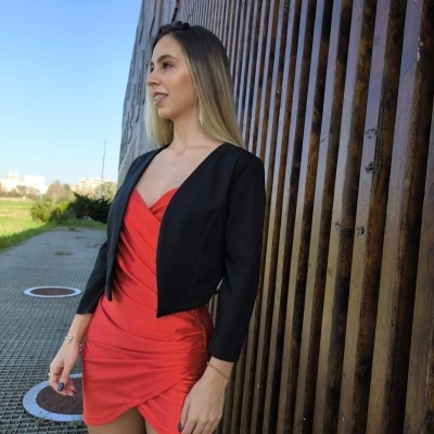 Mulher com vestido vermelho justo e casaco curto preto ao ar livre junto a parede de madeira