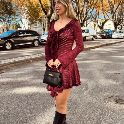 Mulher com vestido bordô de malha e bota preta em rua com árvores outonais