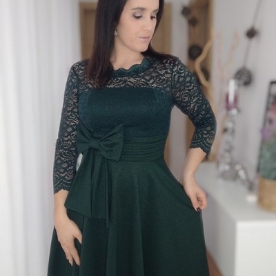 Vestido verde escuro com renda e laço usado por mulher em ambiente interior
