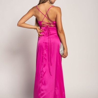 Mulher de costas a usar vestido comprido rosa fúcsia com alças cruzadas e mala prateada