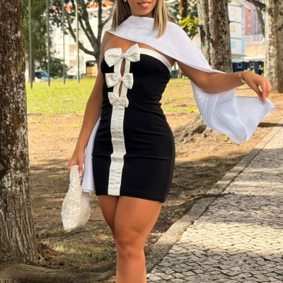 Mulher com vestido preto e branco com laços, lenço branco, sapatos e bolsa brancos num parque