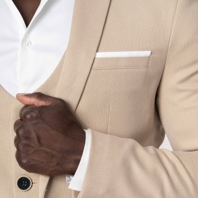 Homem veste casaco bege com camisa branca e lenço branco no bolso ao peito.