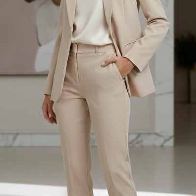 Mulher vestindo blazer bege, calças bege e sapatos de salto alto bege com blusa branca em ambiente interior moderno.