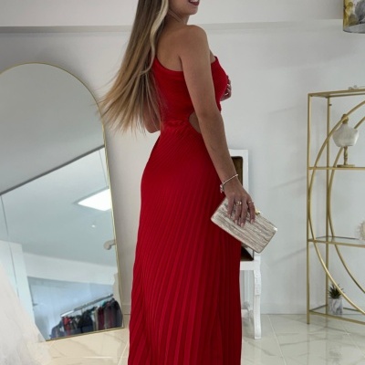 Mulher com vestido longo vermelho plissado e clutch bege em ambiente interior moderno