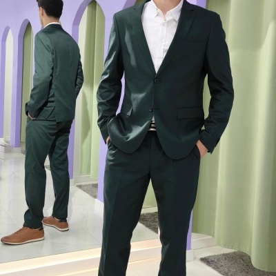 Homem com fato verde escuro, camisa branca e sapatos castanhos em ambiente interior com decoração floral