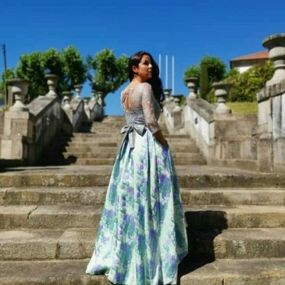 Mulher com vestido longo azul claro floral e renda cinzenta em escadaria de pedra