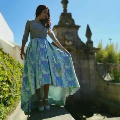 Mulher vestindo vestido comprido cinzento e azul floral com sapatos de salto altos azul claro em ambiente exterior com monumento de pedra