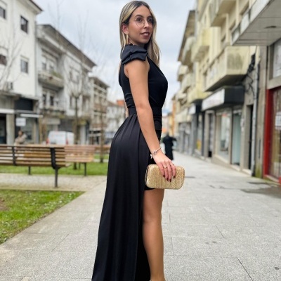 Mulher de vestido longo preto e mala bege em rua urbana