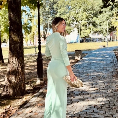 Mulher de vestido verde claro com capuz e mala dourada numa calçada de pedra