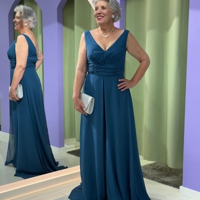 Mulher com vestido azul-petróleo longo e carteira prateada em ambiente com espelho e paredes coloridas