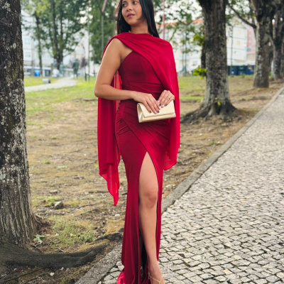 Mulher com vestido longo vermelho e mala clutch dourada num passeio com árvores.