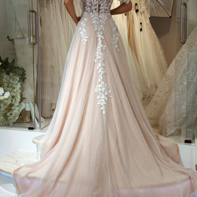 Vestido de noiva rosa claro com bordados brancos nas costas e ombros, visto de trás, em loja de vestidos de noiva.