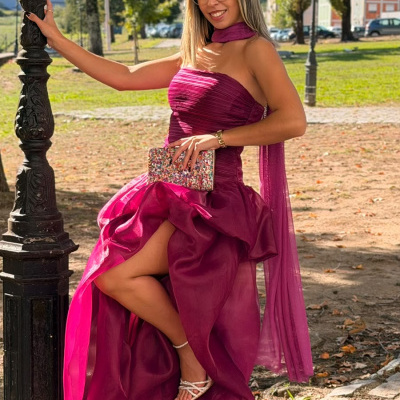 Mulher sorridente com vestido magenta longo em parque, segurando uma lanterna preta.