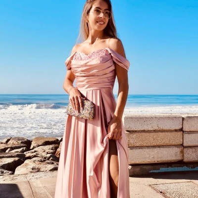 Mulher com vestido longo rosa claro e clutch junto ao mar