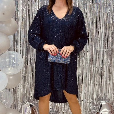 Mulher com vestido azul escuro com lantejoulas e clutch azul brilhante em cenário festivo prateado.