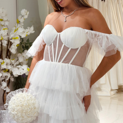 Vestido de noiva curto branco com corpete estruturado e tule, modelo a sorrir com óculos e bouquet branco.