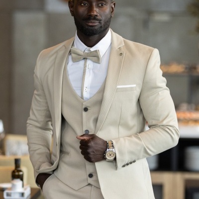 Homem de fato bege com gravata borboleta e relógio em ambiente interior moderno